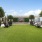 green lawn with two sets of adirondack chairs on either side next to large potted trees and a TV in the middle of the lawn
